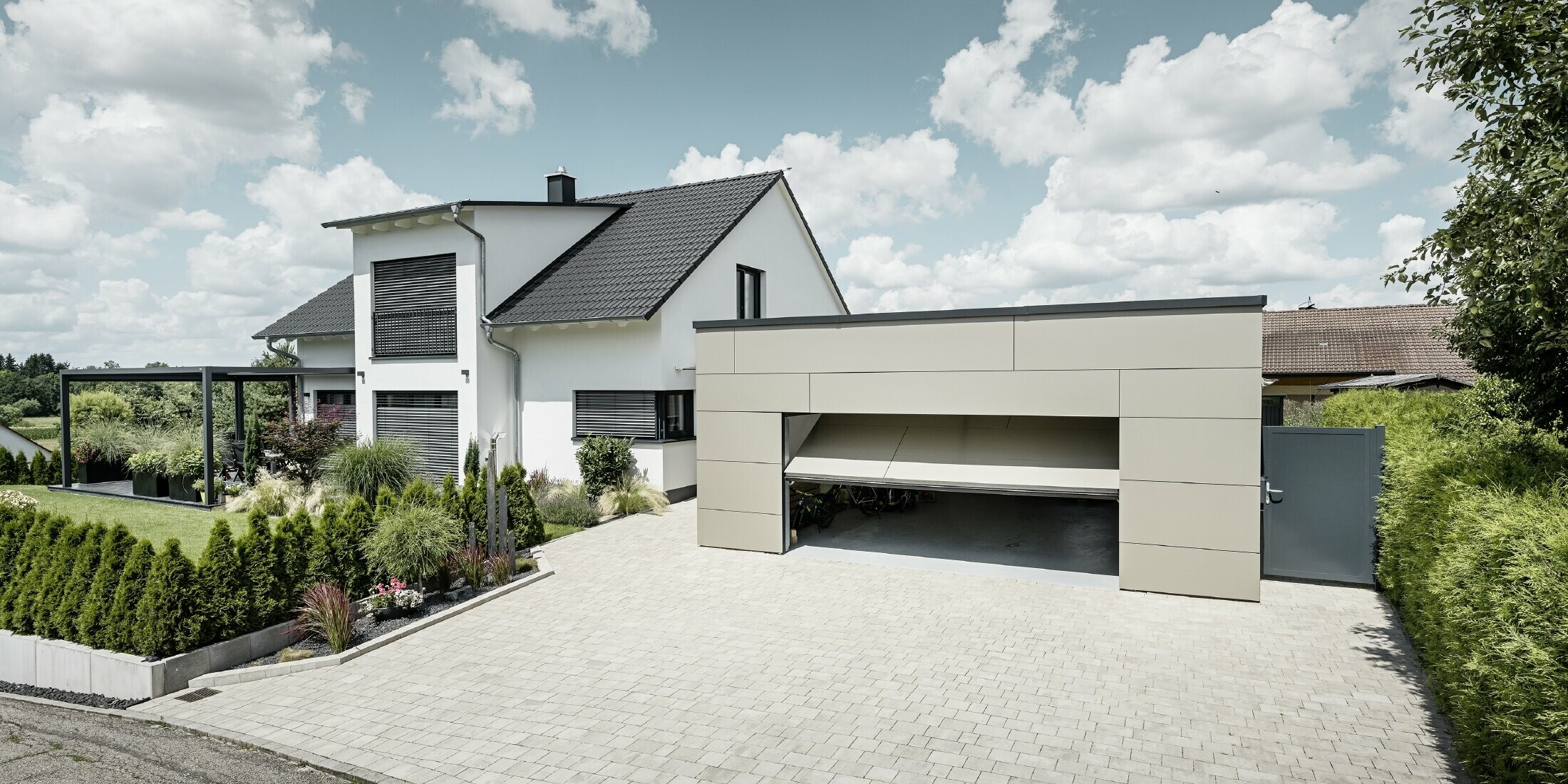 Die Fassade der Garage des Einfamilienhauses wurde komplett mit der PREFABOND Aluminium Verbundplatte in Bronze verkleidet. Das Garagentor ist geöffnet, davor ist eine große Einfahrt für mindestens 2 Autos gepflastert. 