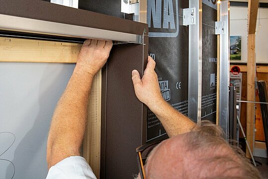 Nahaufnahme eines Fensters, bei dem die seitliche Laibung durch einen PREFA Techniker eingepasst wird.