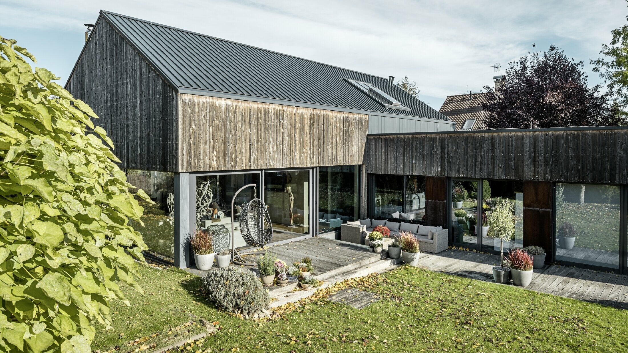 Einfamilienhaus mit Satteldach, eingedeckt mit Doppelstehfalz PREFALZ in Anthrazit und verwitterter Holzfassade. Mit schöner Holzterrasse und großen Fensterflächen im Erdgeschoss.