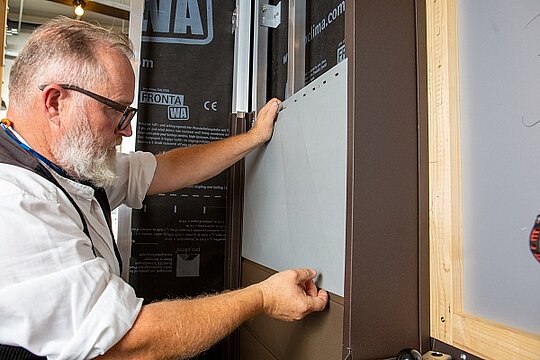 Der letzte Schritt der Anbringung eines Siding-Elements an einer Fassadenvorrichtung wird gezeigt.  Ein letzter Kontrollblick stellt sicher, dass das Siding Element korrekt an der Fassade angebracht wurde.