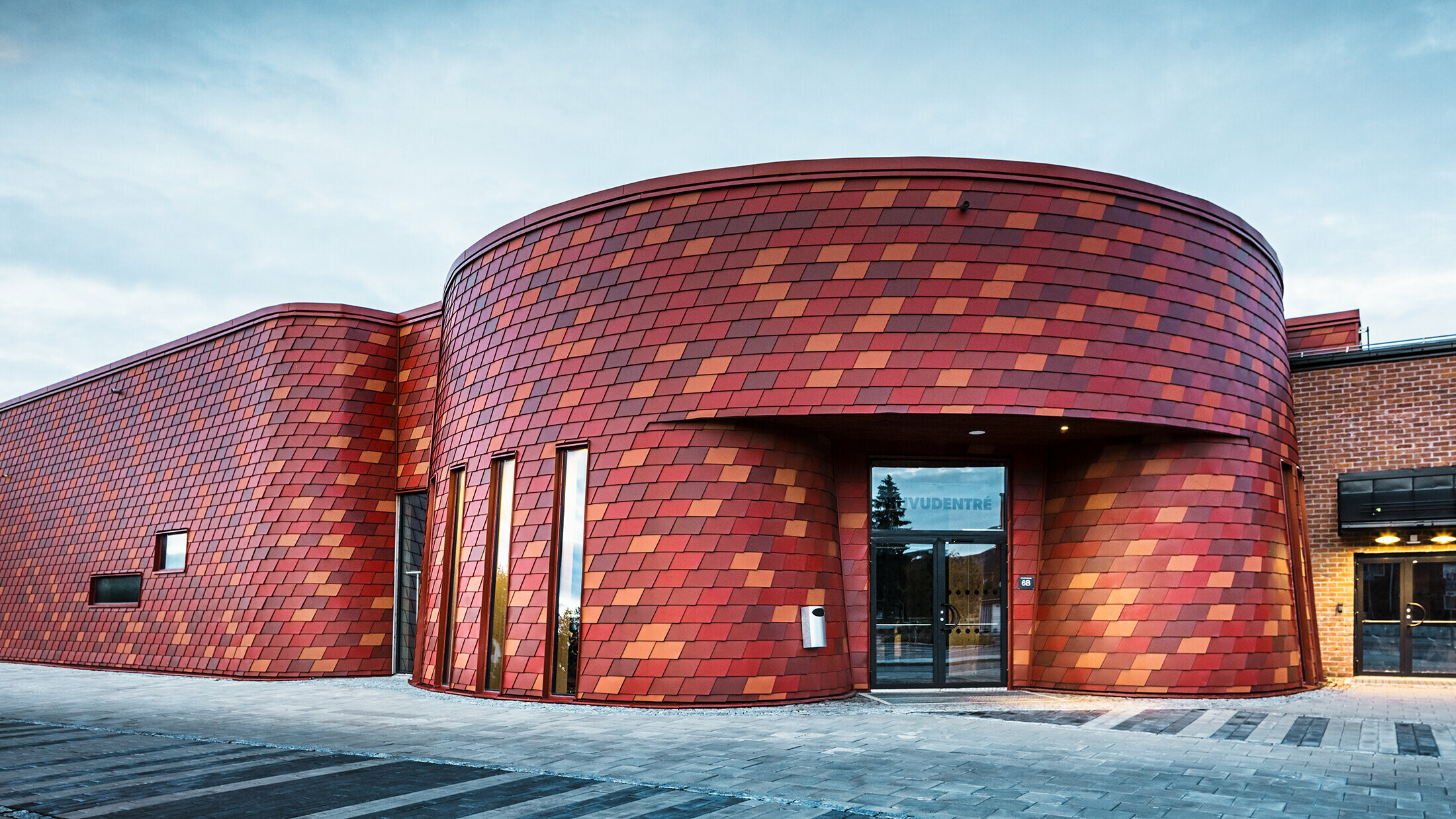 Große Eissporthalle mit abgerundeten Ecken. Die Fassade wurde mit Wandschindeln von PREFA in unterschiedlichen Rottönen verkleidet.