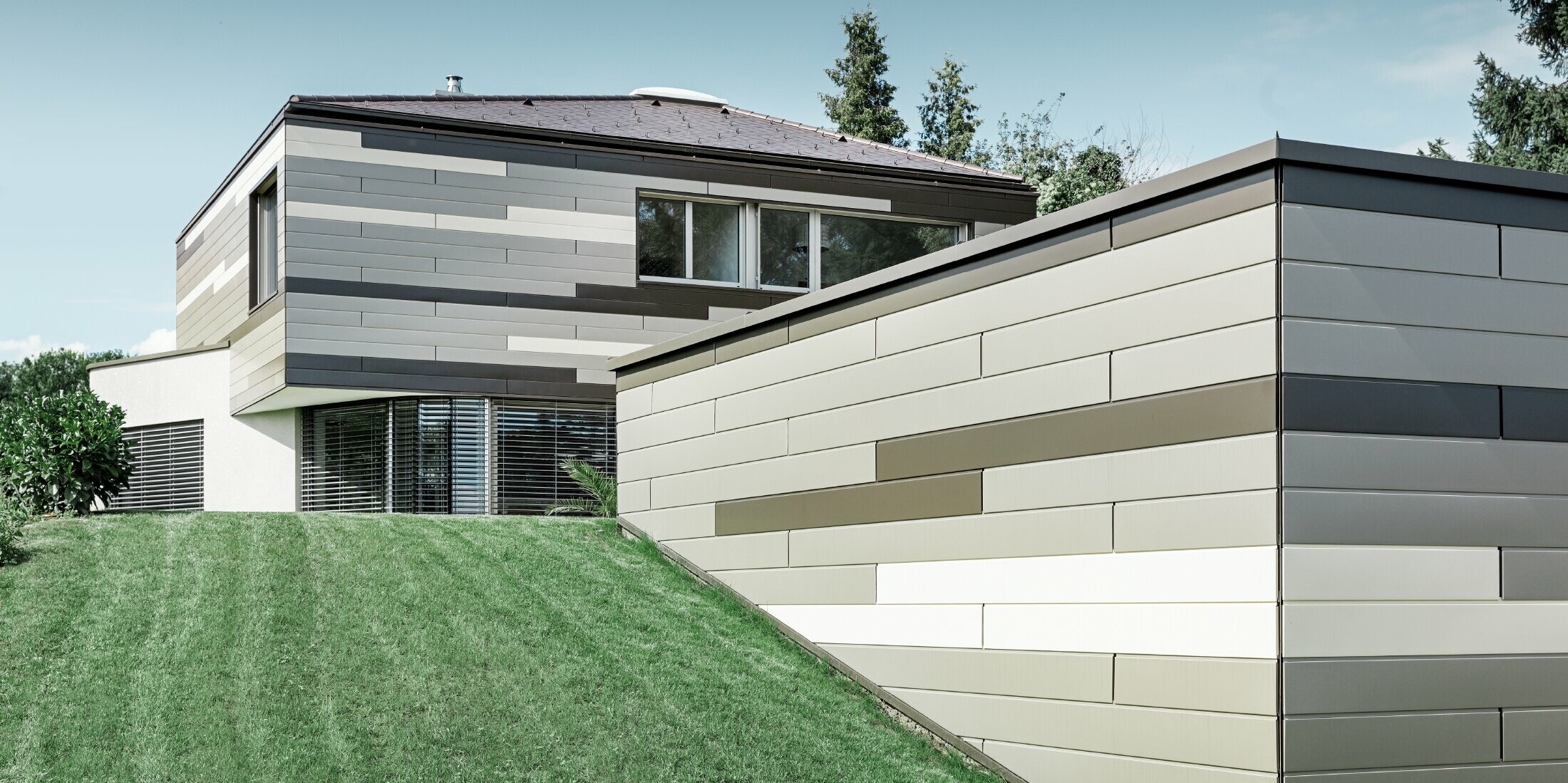 Modernes Einfamilienhaus mit Flachdach und überdachter Terrasse mit einer individuell gestalteten Aluminiumfassade aus Sidings in braun, bronze und elfenbein von PREFA