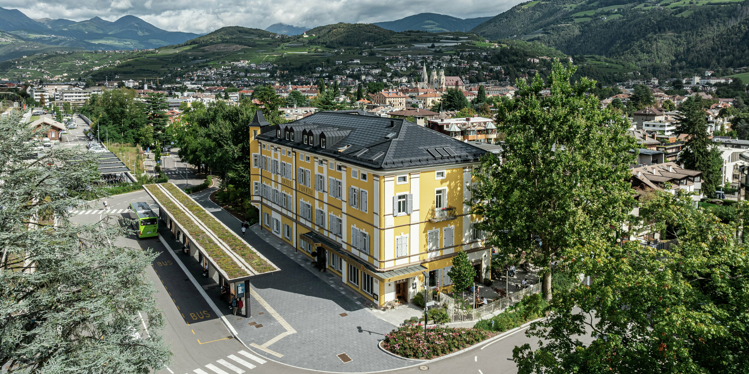 Panoramablick auf das Hotel Jarolim in Brixen, ausgestattet mit einem modernen PREFA Dach aus Solardachplatten und Dachplatten R.16. Das langlebige und witterungsbeständige Aluminiumdach verbindet nachhaltige Energiegewinnung mit eleganter Ästhetik und fügt sich harmonisch in die denkmalgeschützte Architektur des Gebäudes ein. Umgeben von der malerischen Südtiroler Landschaft zeigt das Hotel, wie sich Tradition und Innovation perfekt verbinden lassen.