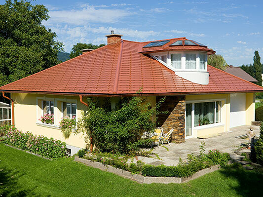 Einfamilienhaus mit Walmdach und Gaube, gedeckt mit PREFA Aluminiumschindeln in ziegelrot.