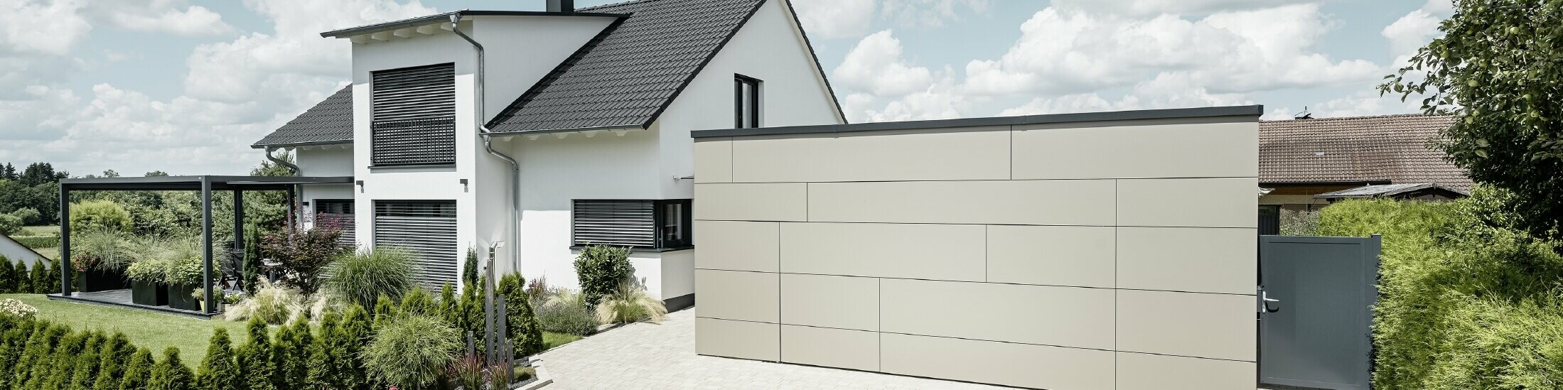 Die Garage des Einfamilienhauses ist an der Fassade komplett mit der Aluminium Verbundplatte in Bronze verkleidet. Auch das Garagentor ist mit den Fugen nicht erkennbar. Davor ist eine großzügige Einfahrt. 