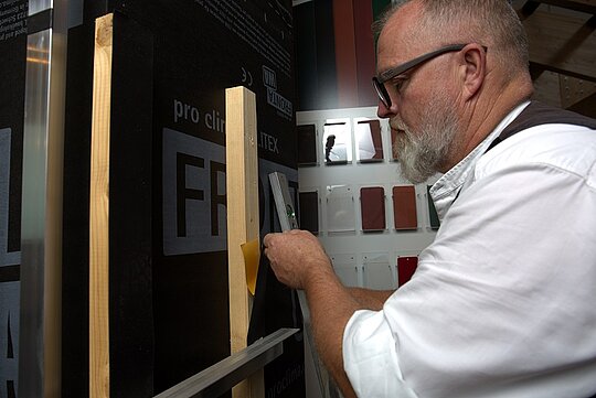 PREFA-Techniker Tom Weiß befestigt ein schwarzes EPDM-Fugenband mit einem Tacker auf einer Holzunterkonstruktion.