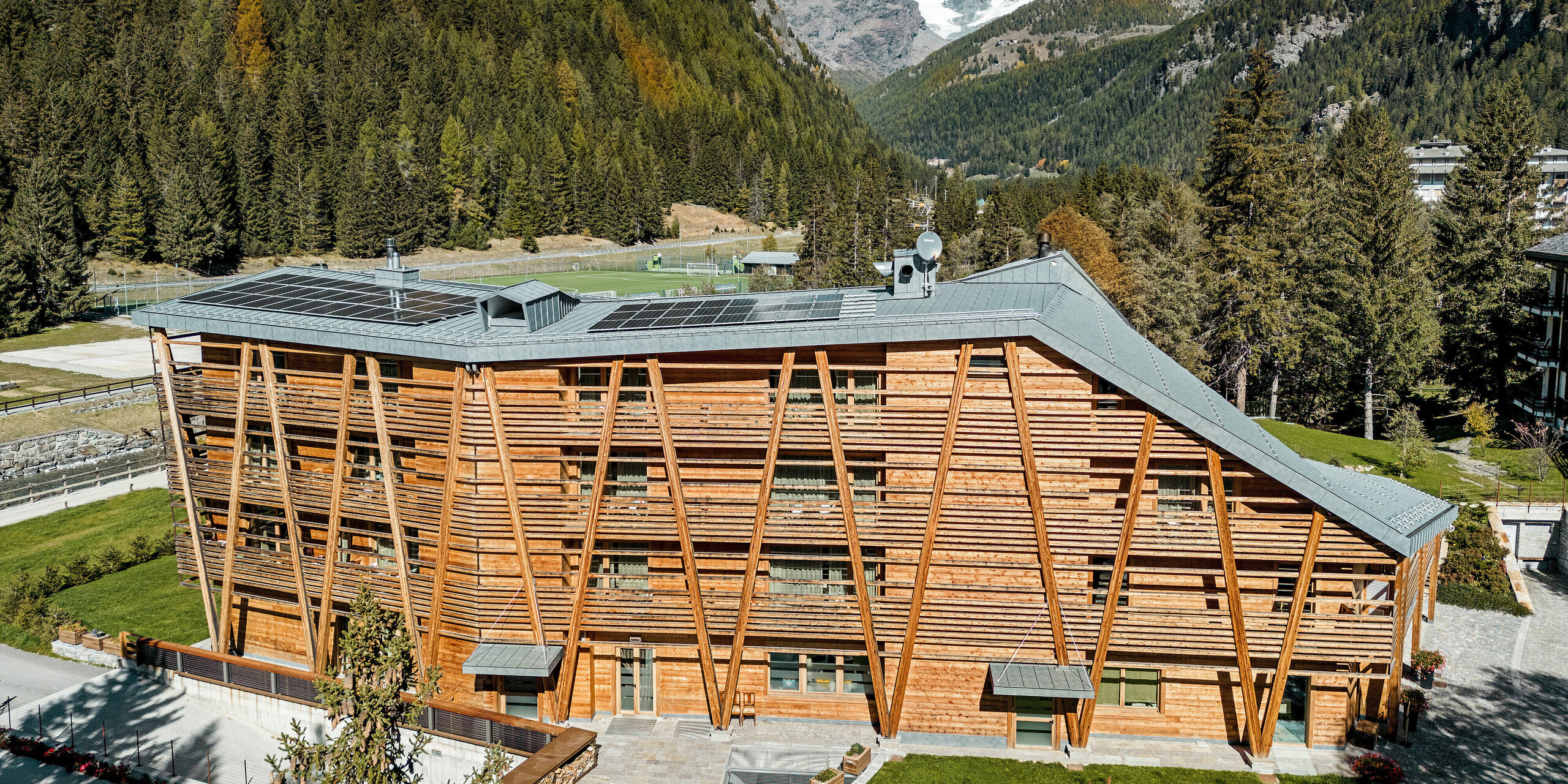 Das Hotel 'Au Charmant Petit Lac' in Champoluc präsentiert sich mit seiner charakteristischen Holzfassade und einem PREFALZ Aluminiumdach in P.10 Steingrau, das durch die Integration von Solarmodulen eine umweltbewusste Energiegewinnung ermöglicht. Die Konstruktion fügt sich harmonisch in die alpine Umgebung ein und spiegelt die Verpflichtung des Hotels zu Nachhaltigkeit und natürlicher Ästhetik wider. Die klaren Linien des Daches und die natürliche Textur der Holzelemente erzeugen eine visuelle Synergie, die Modernität und Tradition vereint.