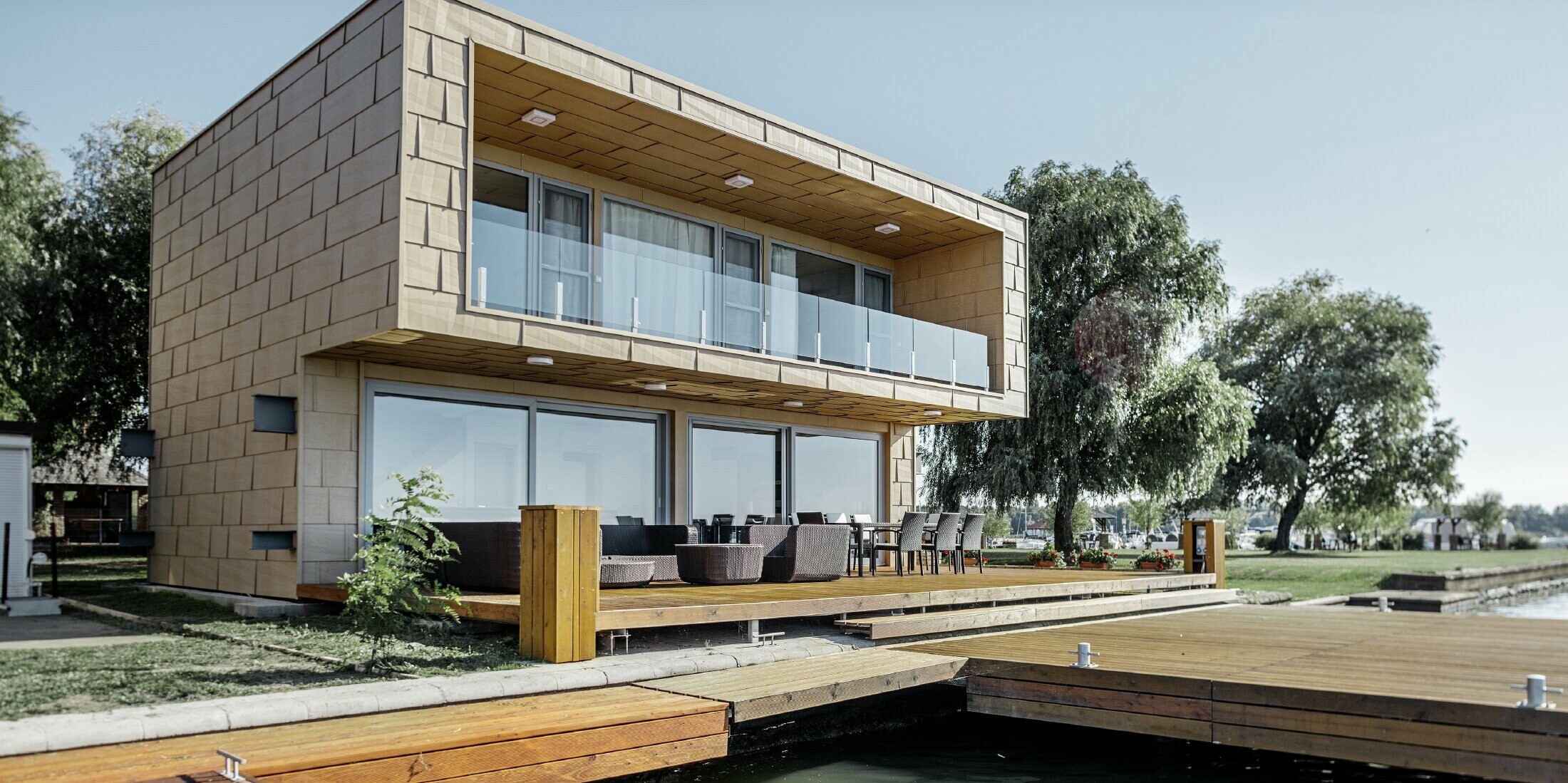 modernes Wochenendhaus mit Flachdach und großen Fensterflächen am See mit einer gekanteten Aluminiumfassade in sandbraun