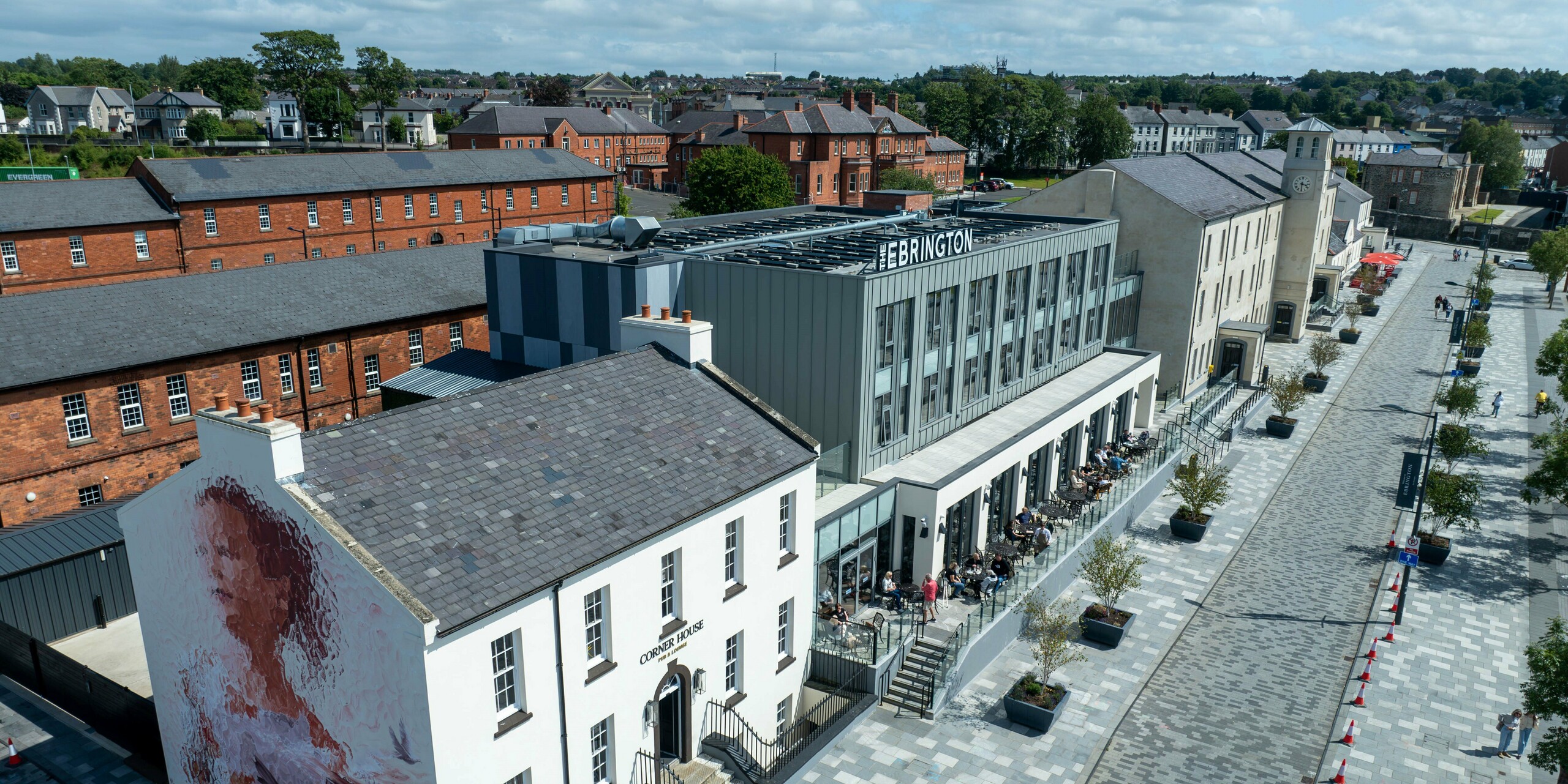 Das Ebrington Hotel im Zentrum von Londonderry, Nordirland, beeindruckt mit seiner modernen PREFALZ-Blechfassade in P.10 Hellgrau und P.10 Zinkgrau. Diese stilvolle und hochwertige Verkleidung von PREFA verleiht dem Gebäude eine elegante Optik und robusten Schutz. Das Bild zeigt auch die Umgebung mit historischen Gebäuden, die einen interessanten Kontrast zur zeitgenössischen Architektur des Hotels bieten. Die langlebige Aluminiumfassade sorgt dauerhaft für eine ästhetische Außenansicht.