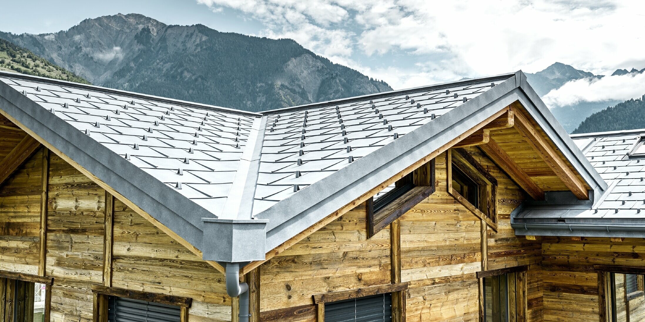 Dach einer rustikalen Hütte in der Schweiz mit Holzfassade und einem Aludach von PREFA. Verlegt wurde die Dachplatte R.16 in Steingrau. Man erkennt das verwinkelte Dach und die Kehle.