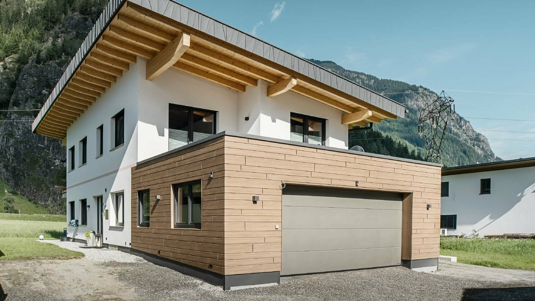 Garage eines Wohnhauses mit PREFA Sidings in Holzoptik im Farbton "Walnuss Braun". Im Hintergrund sind Berge zu sehen. 