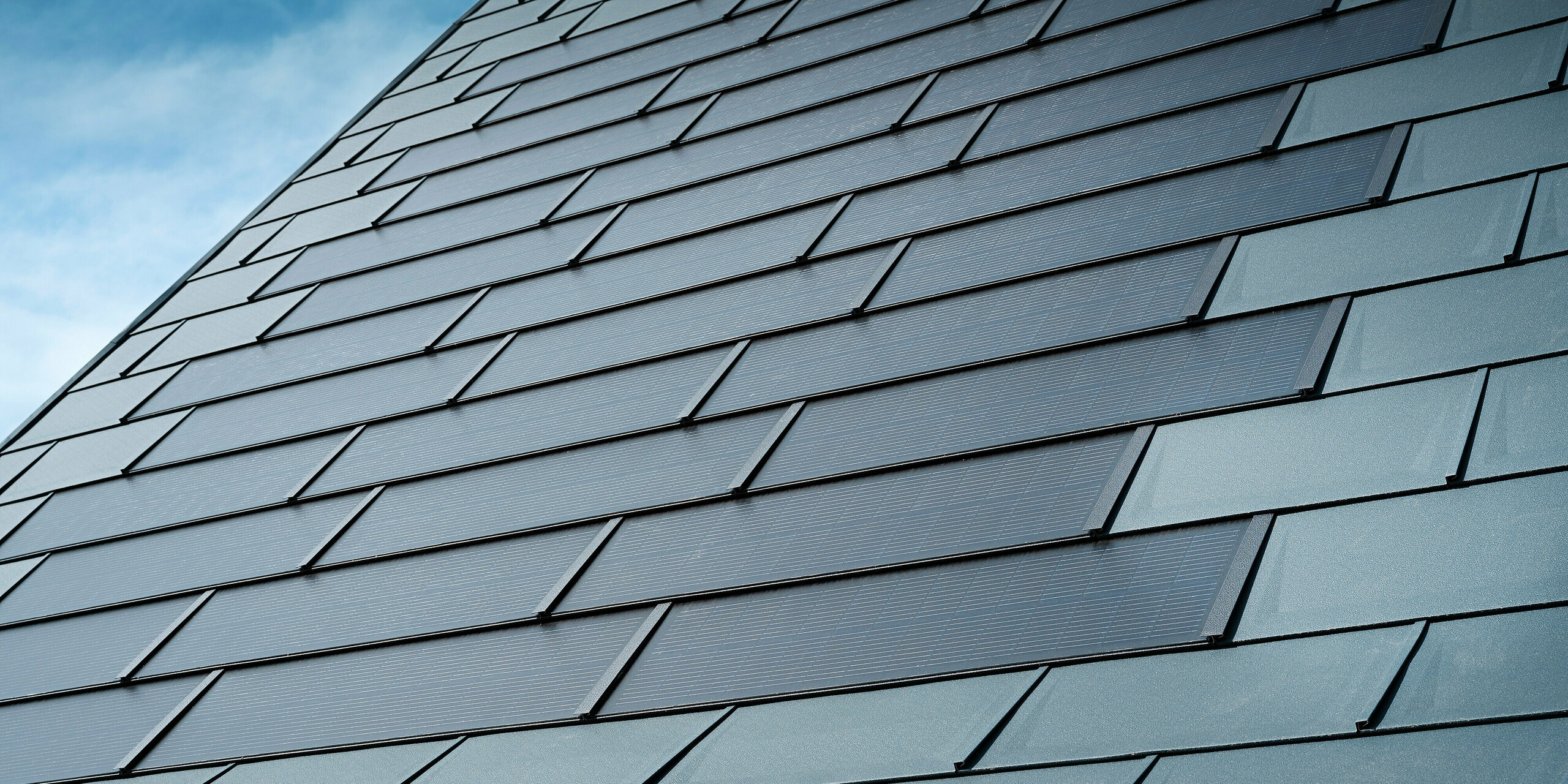 Detailansicht des sanierten Dachs eines Einfamilienhauses in Leonding mit PREFA Solardachplatten in Anthrazit. Die Nahaufnahme zeigt die hochwertigen Blechplatten von PREFA, die eine nahtlose Integration der Solarmodule ermöglichen. Diese langlebige und witterungsbeständige Lösung bietet eine nachhaltige und energieeffiziente Möglichkeit zur Stromerzeugung. Das Bild verdeutlicht die ästhetische und funktionale Qualität der verwendeten Aluminiumbleche. Rund um die innovativen Solardachplatten wurden klassische Dachplatten R.16 in der gleichen Farbe verlegt.