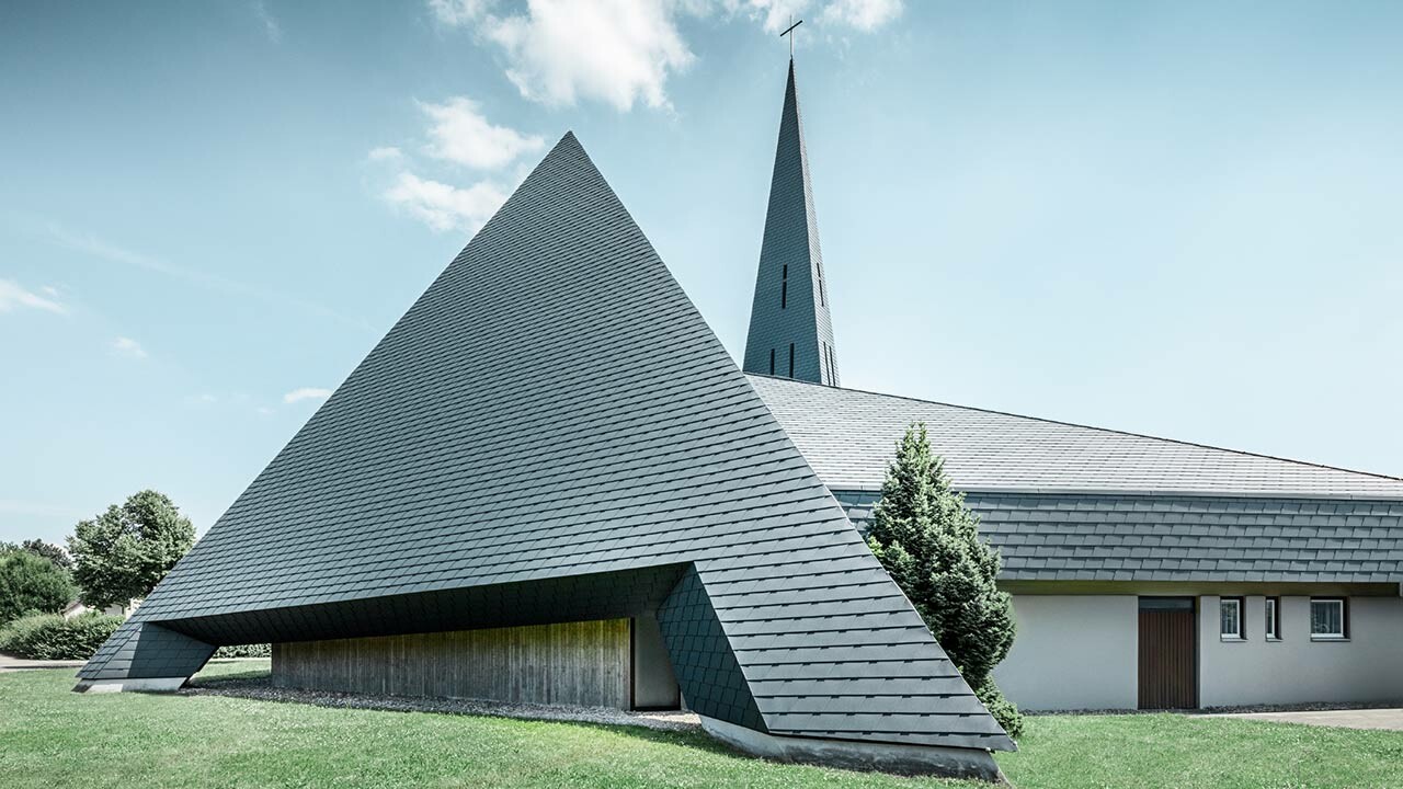 Kirche Langenau in Form einer Pyramide mit einem neuen sturmsicheren Aluminium Dach von PREFA, mit grüner Wiese und blauem Himmel und vereinzelten Wolken