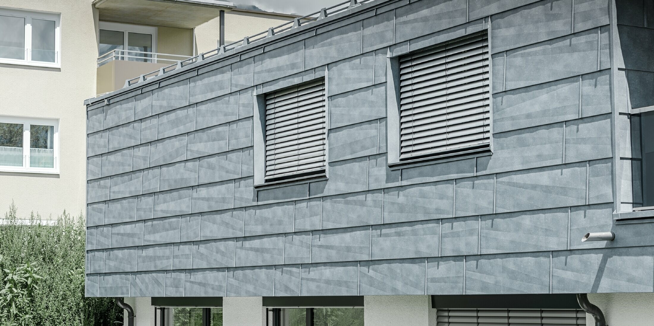 Fassadenfläche mit zwei Fenstern; Die Fassade ist mit dem PREFA Fassadenpanel FX.12 in Steingrau bekleidet.