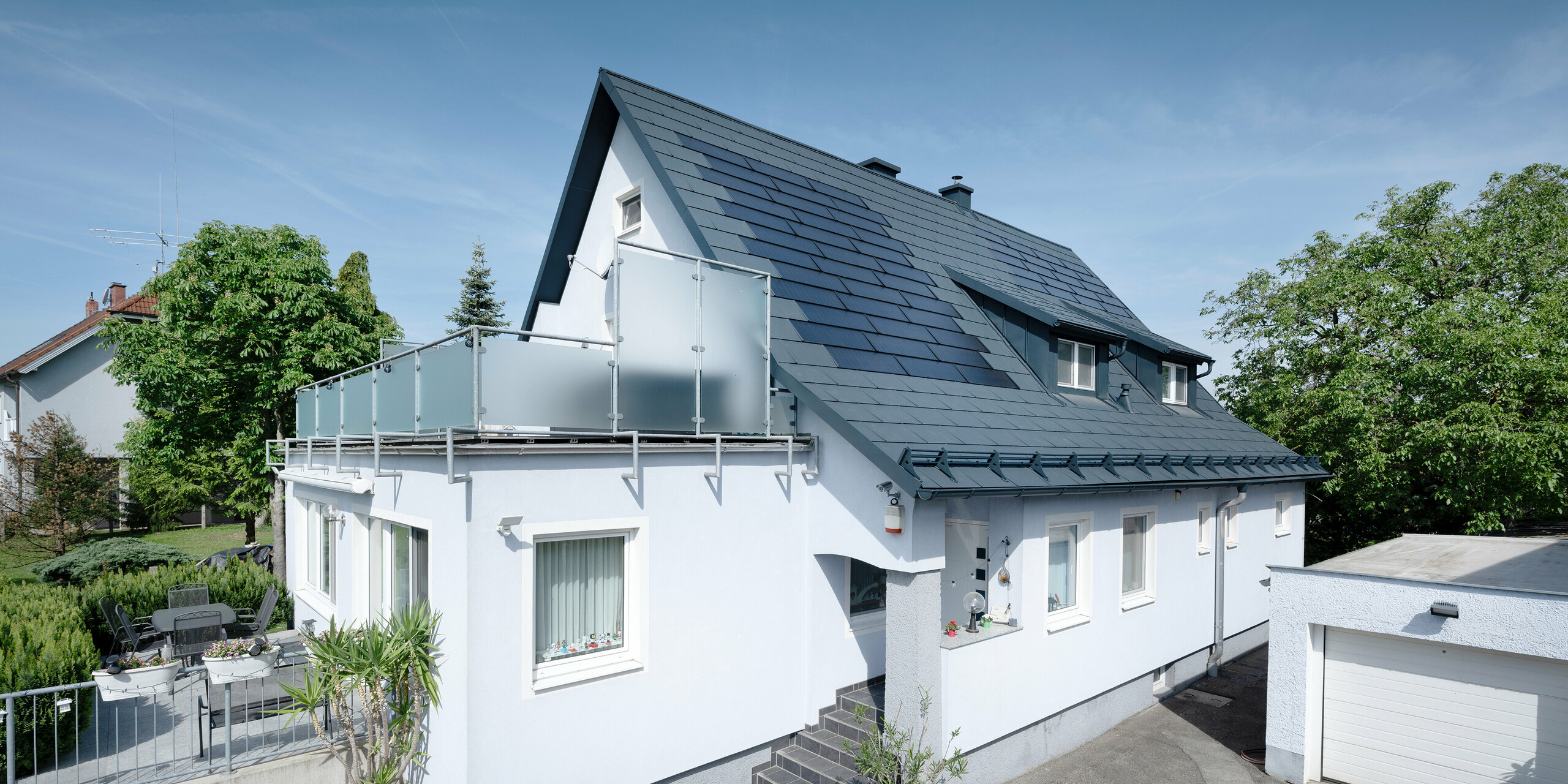 Dachsanierung eines Einfamilienhauses in Leonding mit PREFA Solardachplatten in Anthrazit. Das Bild zeigt das sanierte Haus aus einer seitlichen Perspektive mit klarer Sicht auf das Dach und die integrierten Solarmodule. Diese bieten eine nachhaltige und energieeffiziente Möglichkeit zur Stromerzeugung. Bei diesem Objekt erzeugen die Solardachplatten eine Stromleistung von 10,6 kWp. Die modernen, langlebigen und witterungsbeständigen PREFA Materialien tragen zu einer ästhetischen und funktionalen Dachkonstruktion bei, die den neuesten Standards für nachhaltiges Bauen entspricht.