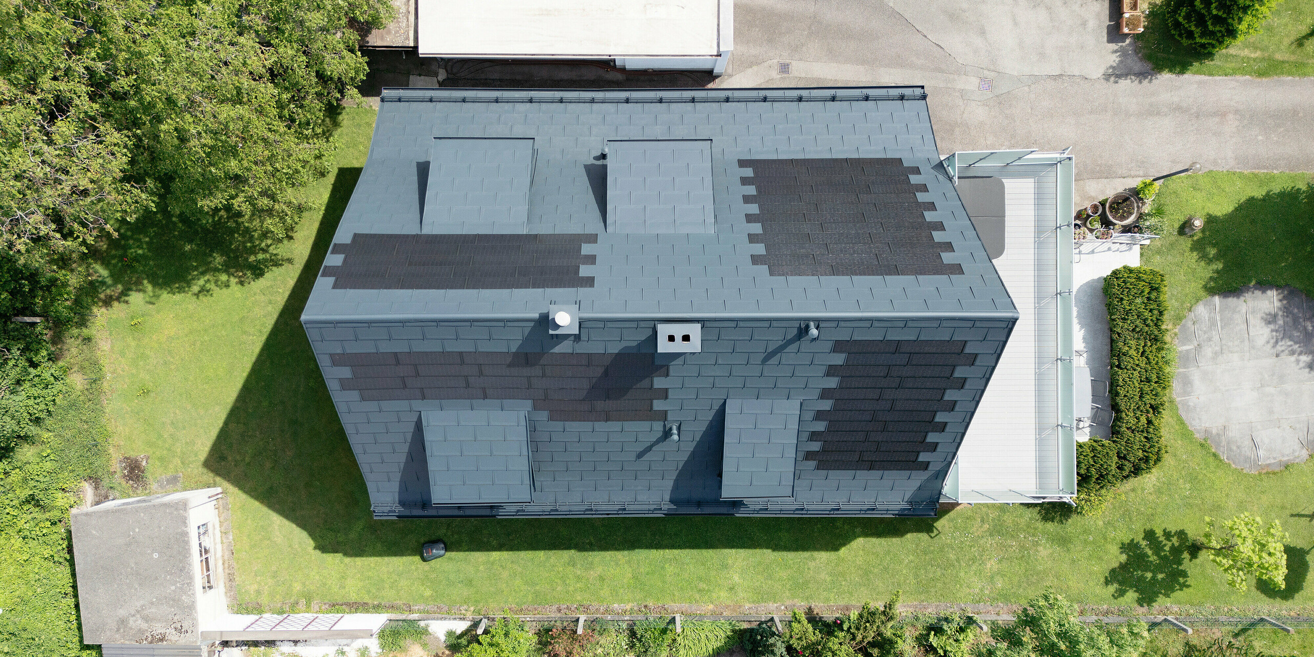 Sanierung eines Einfamilienhauses in Leonding mit PREFA Solardachplatten in Anthrazit. Die Vogelperspektive zeigt das Dach nach der Sanierung, ausgestattet mit integrierten Solarmodulen. Diese bieten eine nachhaltige und energieeffiziente Lösung, die sich harmonisch in die Dachfläche einfügt. Das Projekt zeigt die Vorteile von PREFA Materialien, die Langlebigkeit und Witterungsbeständigkeit mit modernen Photovoltaiksystemen kombinieren. Ideal für nachhaltiges Bauen und innovative Dachlösungen."
