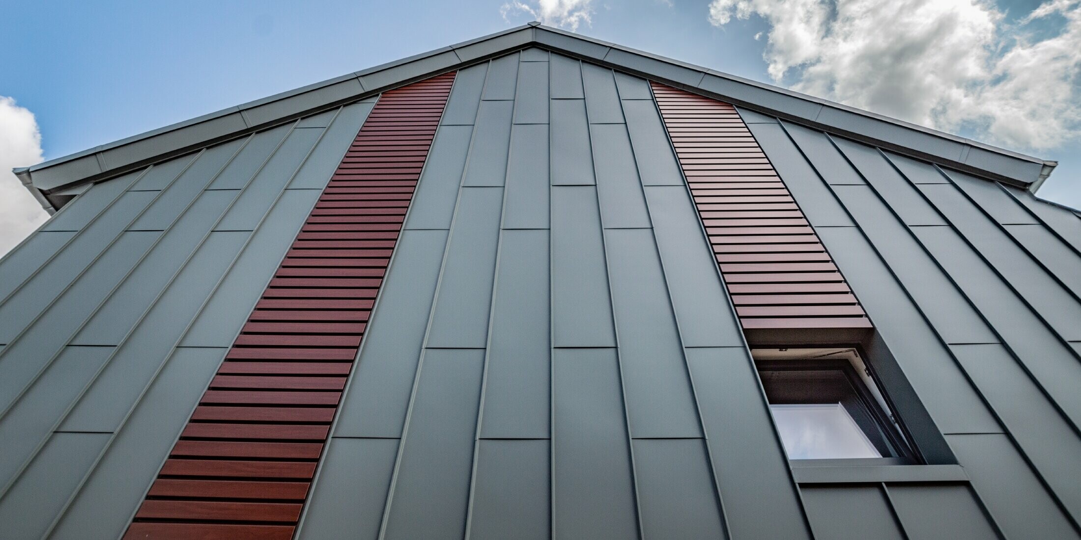 Vertikale Winkelstehfalzfassade mit Tafeldeckung in Hellgrau, sowie Siding horizontal in Holz dunkel von PREFA.