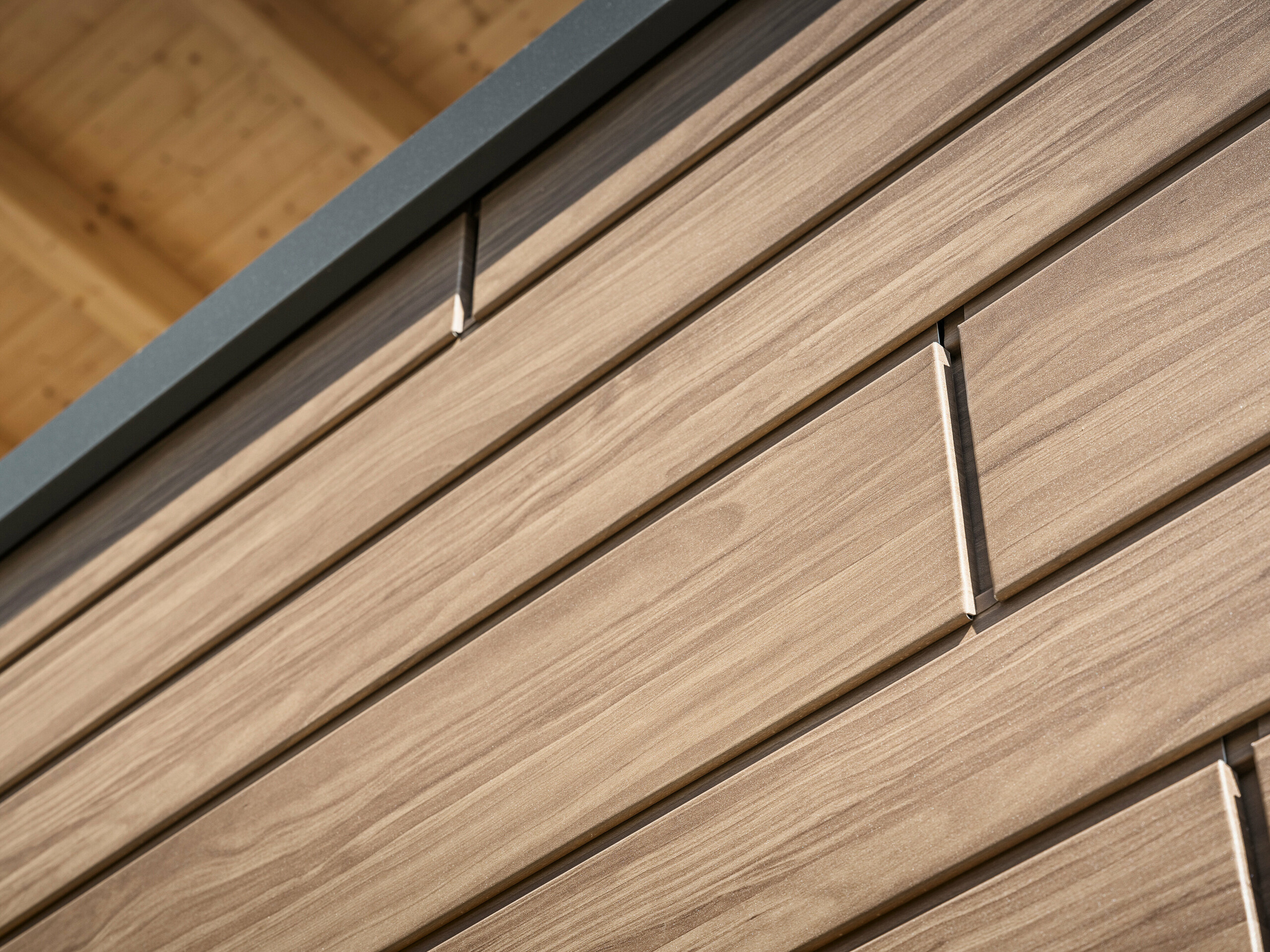 Detailansicht einer Fassadenverkleidung mit PREFA Sidings in Holzoptik. Die Sidings haben eine Materialdicke von 1,2 mm für glatte Oberflächen bis zu einer Breite von 400 mm und 1,5 mm für Breiten von 500 und 600 mm.