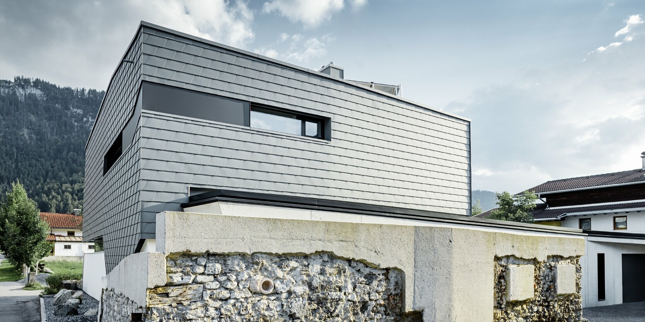 modernes Einfamilienhaus mit Flachdach, großen Fensterflächen und einer Schindel-Fassade in hellgrau aus Aluminium von PREFA