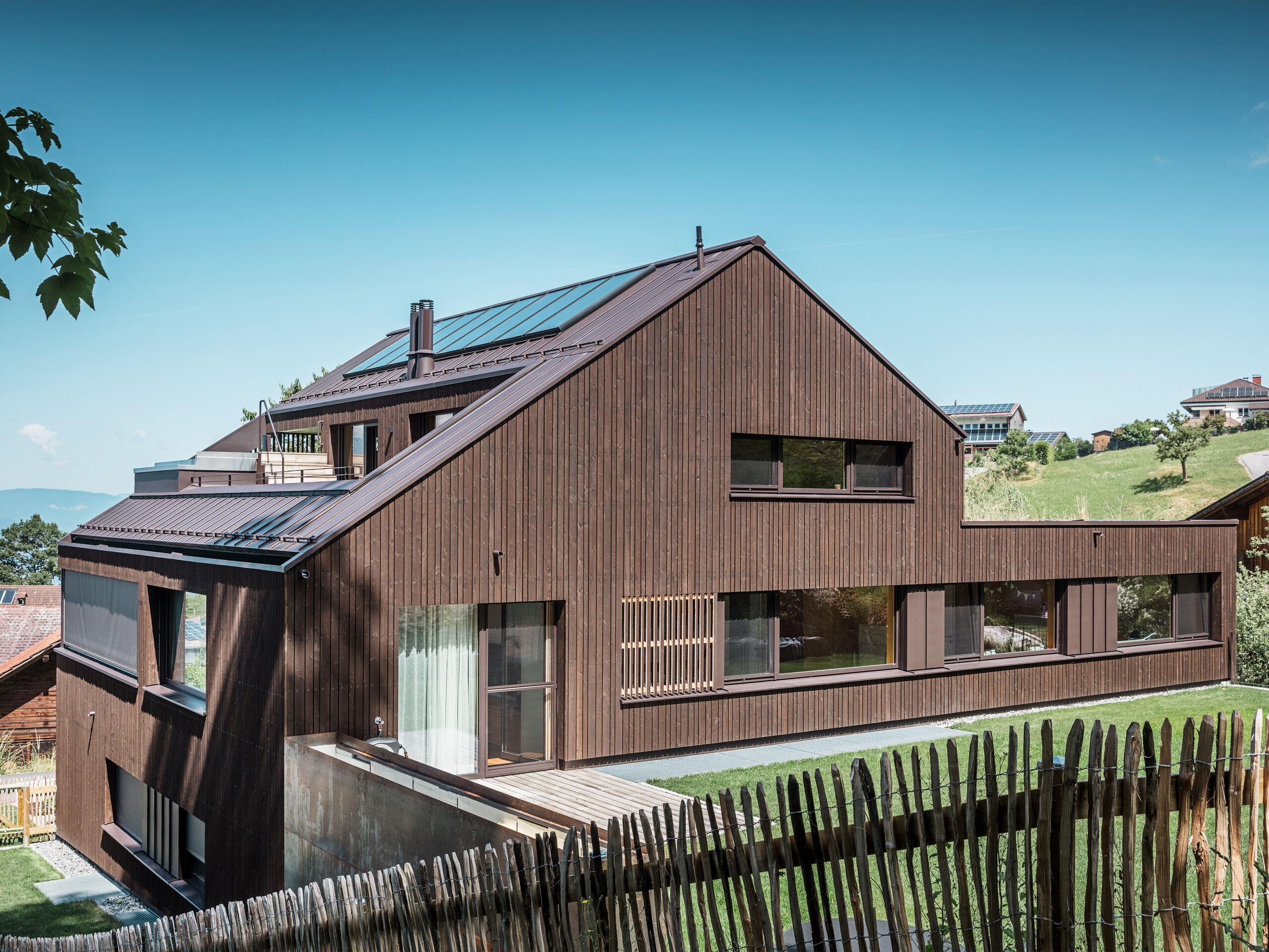 Monochromes Mehrfamilienhaus mit Aluminiumdach und Weißtannenfassade aus seitlicher Perspektive nach dem Umbau.