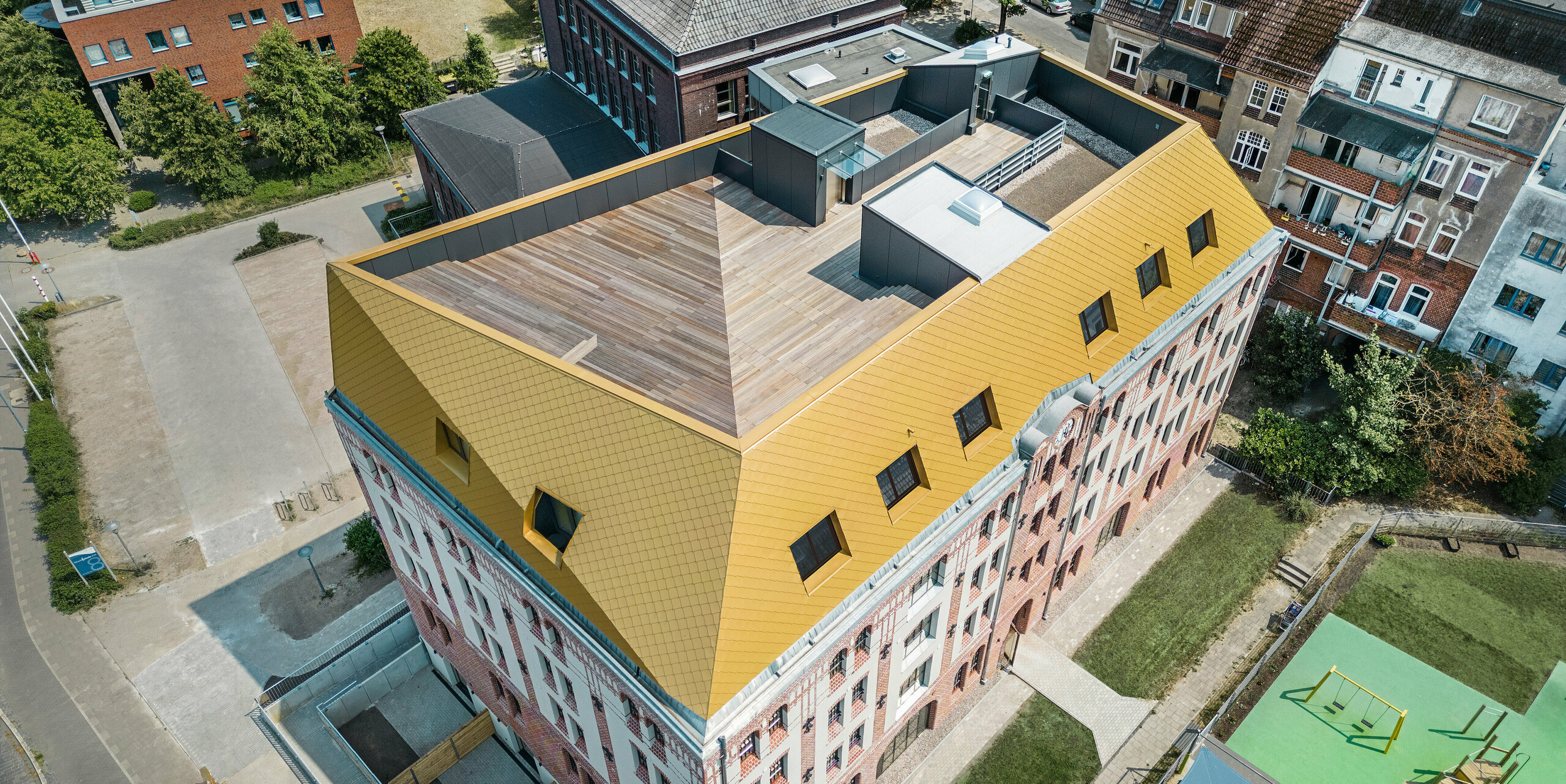 Blick auf das Dach des Studentenwohnheims "The Station" in Kiel. Der Blick von oben zeigt die edlen Aluminiumrauten von PREFA in der Farbe Mayagold am Dach des Gebäudes mit der geknickten Dachlandschaft.