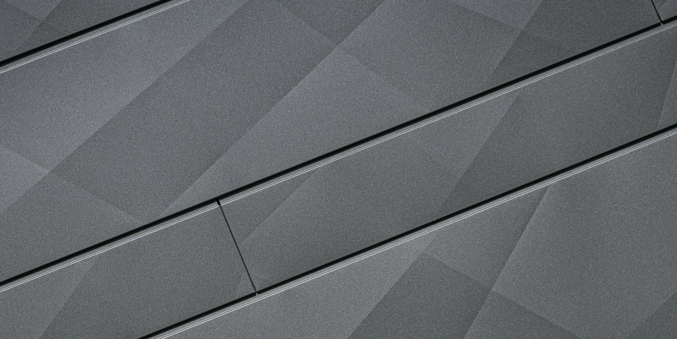 Nahaufnahme der innovativen Siding.X Fassadenpaneele von PREFA in P.10 Dunkelgrau an der Villa Tia in Italien. Die Paneele wurden als Sonderlösung in schräger Ausführung montiert zeigen ein einzigartiges, geometrisches Muster, das die Präzision und Qualität der PREFA Aluminiumprodukte unterstreicht. 