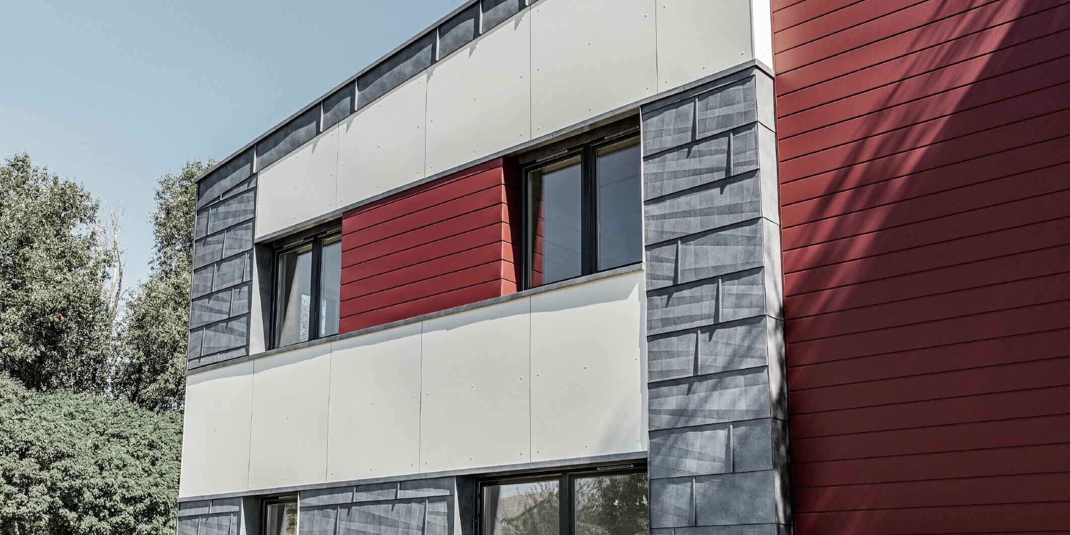 Modernes Bürogebäude mit einer geteilten Fassade in rot, steingrau und weiß mit Aluminiumprodukten Sidings, Fassadenpaneel FX.12 und Aluminium Verbundplatte von PREFA