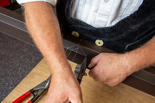 Zu sehen ist unser PREFA Techniker mit einer Aluminiumschere, welcher die Außenecken des Sockelprofils anreißt und ausarbeitet.