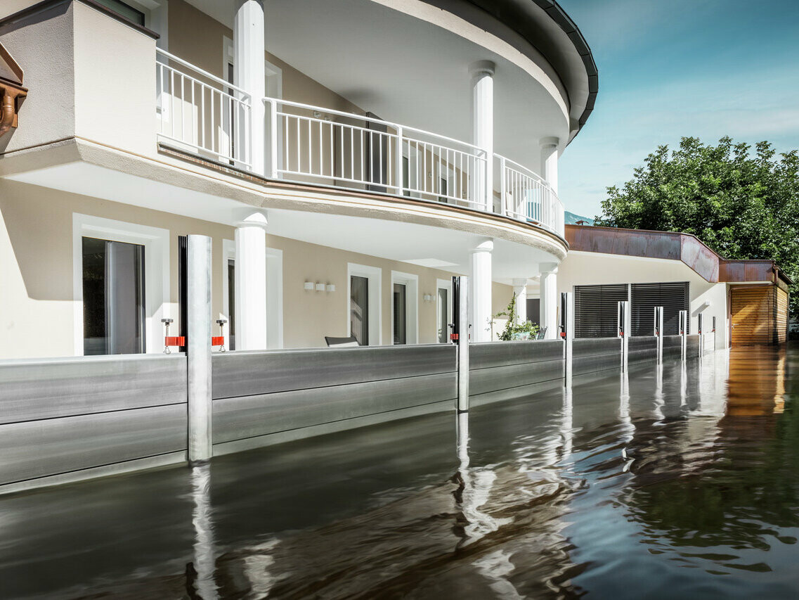 Zu sehen ist ein Einfamilienhaus mit Balkon. Durch den PREFA Hochwasserschutz ist das Haus vor dem bereits steigenden Hochwasser geschützt.