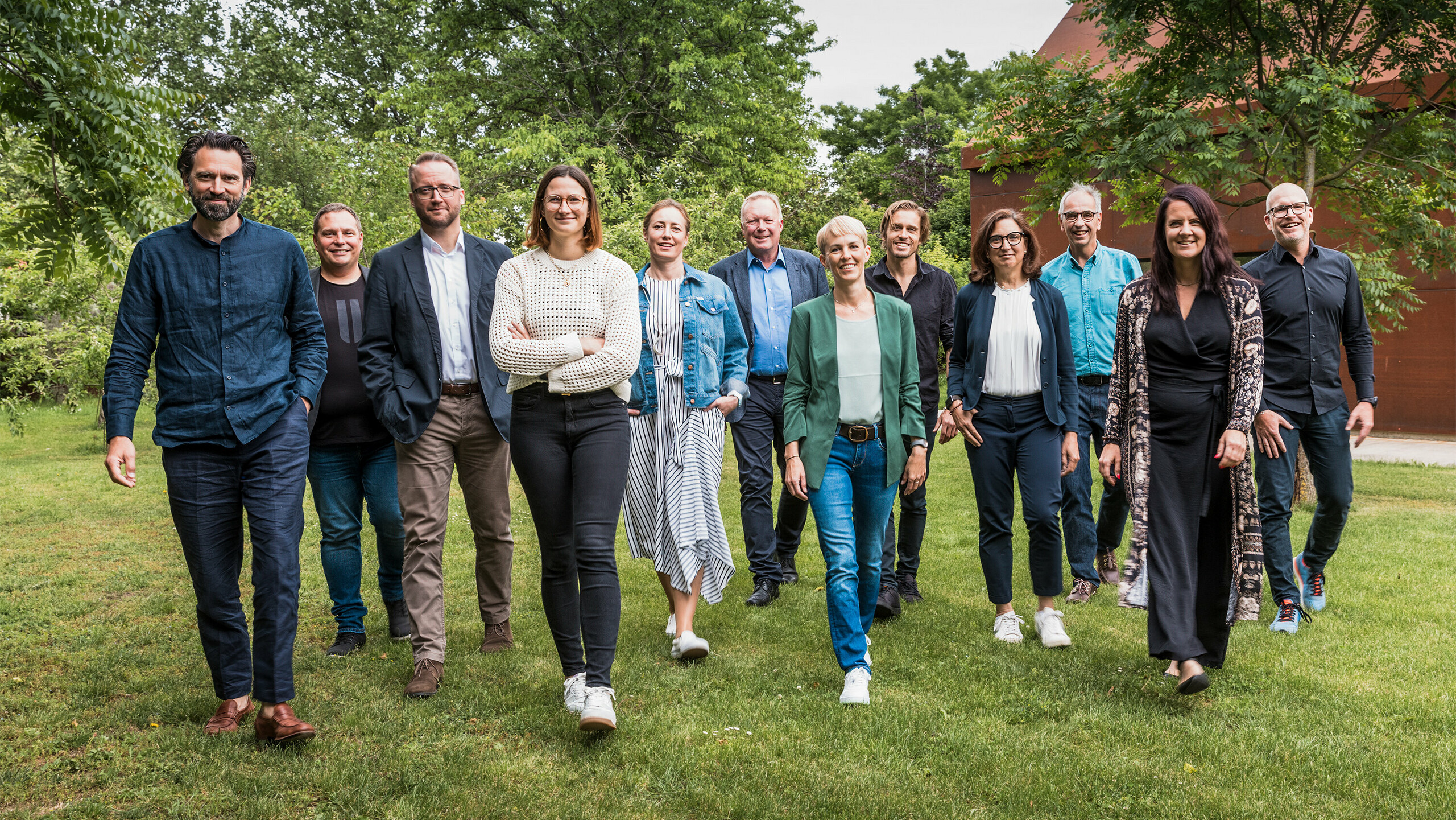 Gruppe von Expert:innen und Architekt:innen beim PREFARENZEN 2025 Dialog: Die Jury besteht aus zehn Architekt:innen und PREFA Expert:innen, die gemeinsam auf einer grünen Wiese vor der Residenz Velich im burgenländischen Seewinkel in eine gemeinsame Richtung gehen. Sie lächeln und gehen frontal auf die Kamera zu. Im Hintergrund ist die üppige Vegetation der Umgebung zu sehen. Das Bild entstand bevor die Jury die spannendsten Architekturobjekte für die PREFA Architekturplattform 2025 auswählte. Beim PREFARENZEN Dialog im Mai 2024 lag der Fokus auf der Funktionalität und Einfachheit sowie dem Mehrwert moderner Architekturobjekte. Auf dem Bild zu sehen v. l. n. r.: Thomas Heil (Co-Gründer, dreiplus Architekten), Jürgen Haller (Baumeister, Jürgen Haller GmbH), Christian Wirth (Leiter Objektberatung, PREFA Österreich), Chiara Desbordes (Head of Content, Architektur Aktuell), Paulina Frey (Marketingleiterin, PREFA Schweiz), Gerald Krebs (Objektberater, PREFA Österreich), Veronika Roll (Marketing PREFA Österreich), Daniel Luckeneder (Associate Partner, laac zt gmbh), Patricia Ezcurra (Architektin, wwa Architekten), Wolfgang Croce (Croce & Wir, Graz), Bettina Almeida (Kommunikationsmanagement, PREFA), Jürgen Jungmair (Marketingleiter International, PREFA).