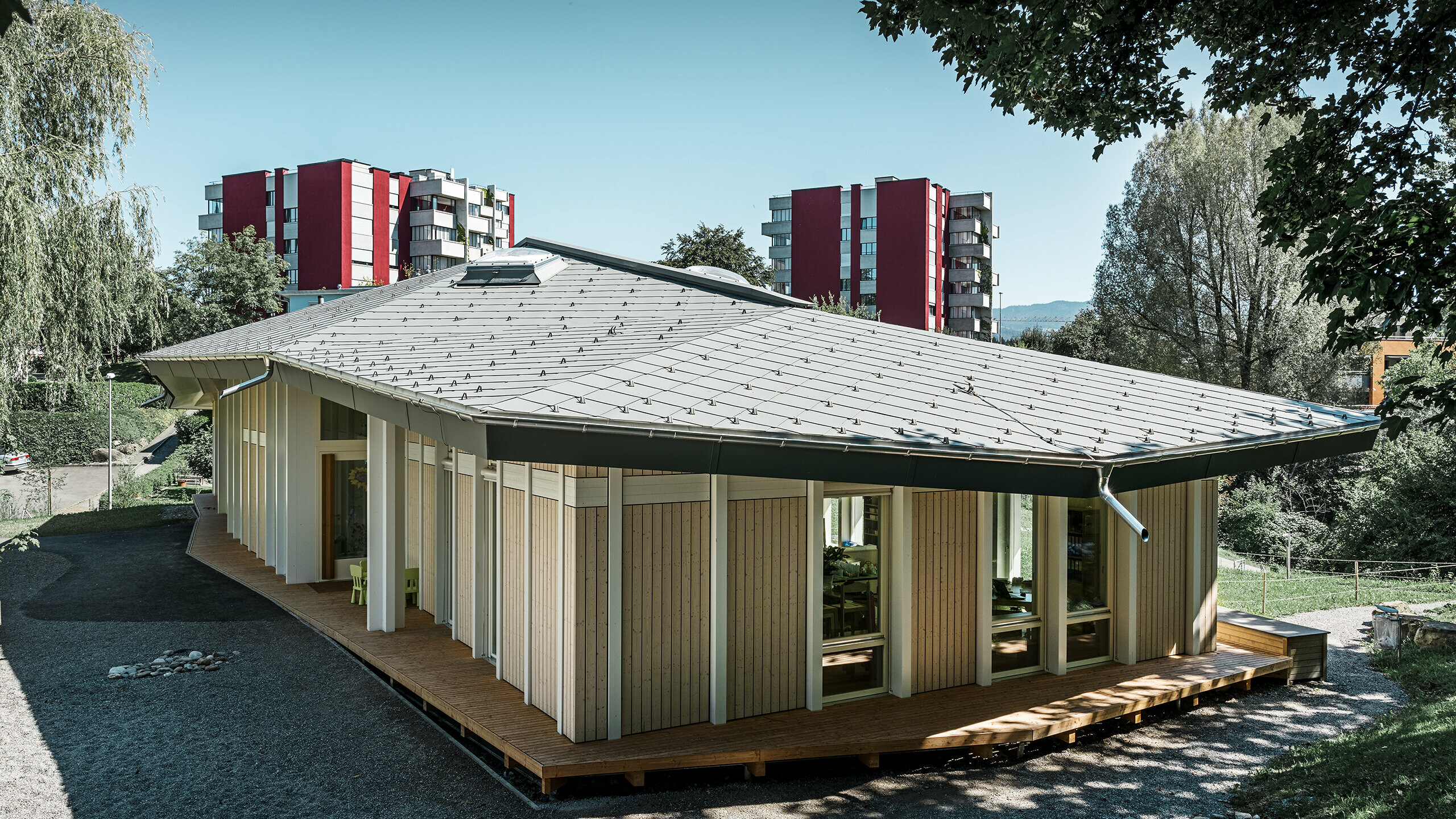 Eingeschossiger Kindergarten mit senkrechten Fassadenpaneelen und Alu-Dach von PREFA (Dachraute) in Hellgrau